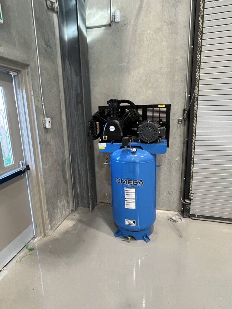 Blue Omega compressor unit installed at an industrial site, positioned on a concrete pad.
