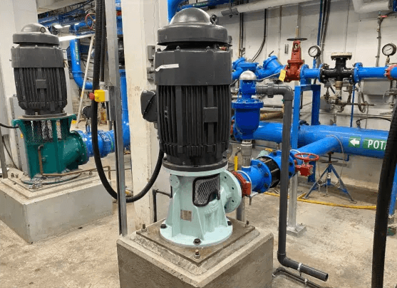 Vertical inline pump installed in an industrial pump room with blue piping and pressure gauges